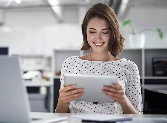 elinde tablet tutarak gülümseyen iş yerinde masada oturan bir kadın