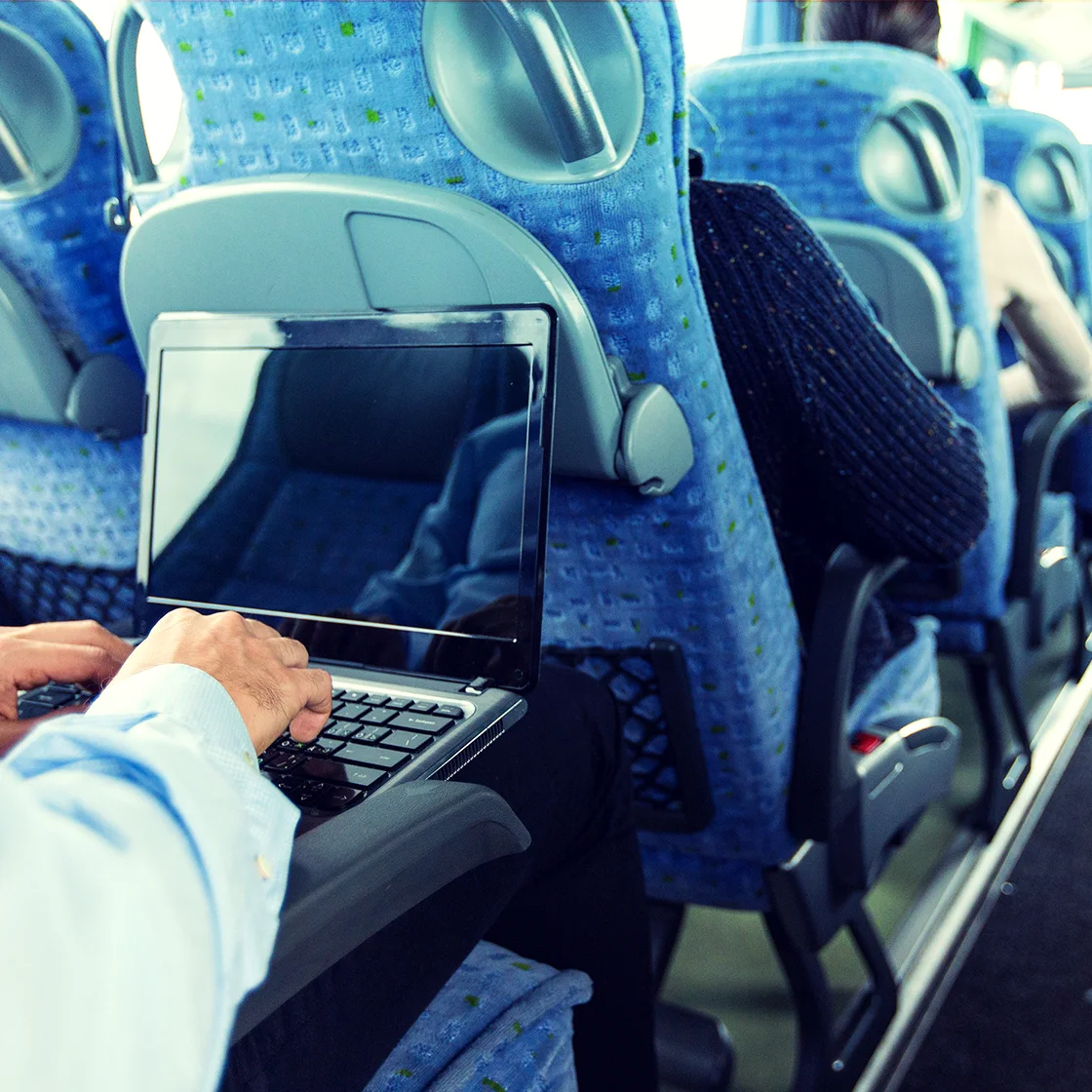 kucağında dizüstü bilgisayar bulunan bir otobüste oturan bir kişi